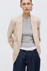 Blazer de sarga color beige, con solapas de pico, frente abierto y bolsillos delanteros ribeteados con solapa.