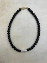 Collar artesanal compuesto por cuentas de piedra volcánica en diversos tonos y tamaños, con una perla natural de río como dije central y cierre metálico dorado.