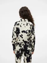 Chaqueta corta con cuello clásico, cierre frontal con cremallera, puños abotonados y estampado de manchas de vaca en blanco y negro.