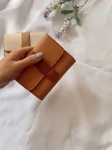 Billetera de cuero sintético con textura granulada, cierre de solapa con broche a presión y tira decorativa central.