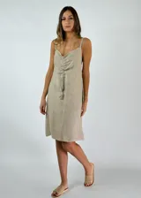 Vestido corto color beige de lino con breteles finos, escote en V y detalle de fruncido con cordón y borlas en el centro del pecho.