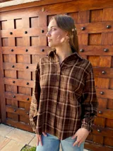 Camisa de manga larga con estampado de cuadros escoceses en tonos marrones. Presenta cuello clásico, cierre frontal con botones y corte holgado.