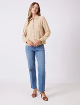 Camisa de crepe color beige con cuello clásico, cierre frontal con botones y dos bolsillos aplicados en el pecho.