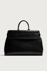 Bolso de mano extragrande negro de cuero sintético, con compartimento principal con cierre de imán, bolsillo interior con cierre y bolsillo secundario con solapa y detalle de cinta. Cuenta con dos asas de mano.