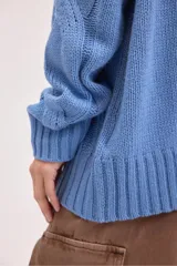 Sweater de punto color azul, con cuello alto y diseño de trenzas verticales. Presenta mangas largas con puños acanalados y un corte holgado.