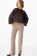 Camisa de corte holgado color marrón chocolate, con cuello clásico, cierre frontal de botones y mangas largas abullonadas con frunces en los hombros.