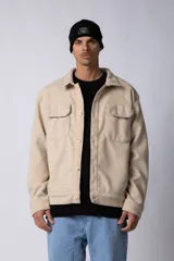 Campera corta tipo sobrecamisa de paño elastizado en color beige, con cuello clásico, cierre frontal de botones veteados y dos bolsillos frontales con tapa.