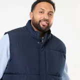 Chaleco acolchado tipo puffer en color azul marino, confeccionado en tejido repelente al agua. Presenta cuello alto, cierre frontal con cremallera y botones a presión, y bolsillos delanteros de parche.