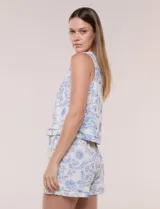 Top crop de lino y viscosa, sin mangas, con escote a la base y estampado floral en tonos azul celeste sobre fondo beige. Cuenta con cierre posterior tipo gota con botón y ruedo recto.