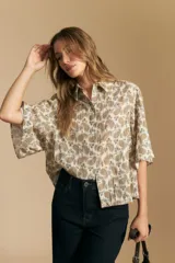 Camisa de manga corta con cuello camisero y estampado paisley en tonos beige, marrón y azul sobre fondo claro. Presenta textura plisada o arrugada en la tela.