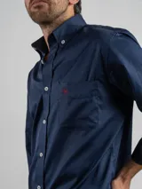 Camisa de corte regular color azul marino, confeccionada en algodón. Presenta cuello con botones, cierre frontal abotonado y un bolsillo en el pecho con el logo de la marca bordado en color rojo.