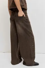 Pantalón de denim estilo wide leg color marrón gastado, con apliques de tachas metálicas o strass distribuidos por toda la prenda y tiro medio.