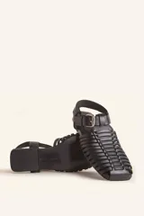 Sandalias planas tipo huarache de cuero negro, con tiras entrelazadas a mano y tira ajustable en el talón con hebilla metálica.