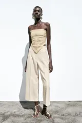 Pantalón de lino negro, de tiro alto, con bolsillos delanteros de vivo, pernera recta y cierre frontal con cremallera, botón interior y gancho metálico.