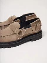 Mocasines Mutma Gales de cuero color tostado, con plataforma gruesa dentada, detalles de tachas metálicas, argollas y tira lateral con hebilla.