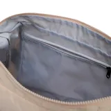 Bandolera de nylon color beige, de diseño holgado y redondeado con bolsillos frontales ajustables con cordón elástico y tope, correa ajustable negra y parche con logo de la marca.