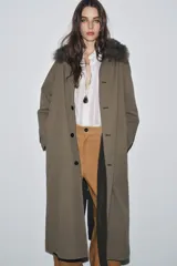 Trench reversible de corte recto con cuello de solapa y aplicación de pelo sintético extraíble. Presenta cierre frontal con botones, manga larga y bolsillos laterales ocultos en las costuras.