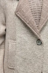 Sacón de diseño amplio con técnica patchwork, confeccionado con retazos de telas de diversas texturas en tonos beige y gris. Presenta mangas ranglan, cuello con solapas y cierre frontal con un único botón.