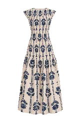 Vestido largo sin mangas de color beige con estampado floral y vegetal en color azul marino. Cuenta con un cuerpo ajustado mediante fruncidos elásticos (smock) y falda larga con vuelo y corte en capas.