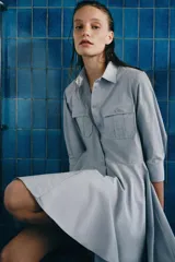 Vestido corto tipo camisero de algodón, con cuello solapa, mangas tres cuartos y cierre frontal con botones. Presenta bolsillos de plastrón con solapa en el pecho y falda con bajo plisado.