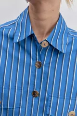 Camisa de corte oversize con diseño de rayas verticales en tonos azul y blanco, cuello clásico, cierre frontal con botones y mangas largas con puños abotonados.