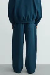Pantalón jogger de corte relajado y pernera ancha, confeccionado en tejido de algodón con interior perchado. Presenta cintura elástica con cordón interior, bolsillos laterales y un bolsillo trasero de plastrón.