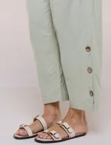 Pantalón de algodón rústico color verde, de tiro medio-alto con pretina elastizada y bolsillos laterales. Presenta corte holgado, diseño cropped de pierna ancha y aberturas laterales en los tobillos con detalles de botones.