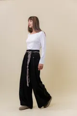 Pantalón wide leg de tiro alto en color negro, con diseño de pinzas delanteras que aportan volumen y caída fluida. Incluye bolsillos laterales y un lazo desmontable en la cintura que combina cordón con cinta de estampado animal print.