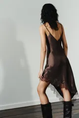 Vestido midi marrón satinado con escote en V, tirantes finos regulables, espalda descubierta con lazo y bajo asimétrico con encaje a tono.