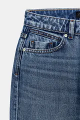 Jeans de tiro alto con diseño de cinco bolsillos, pernera recta y corte largo. Presenta cierre frontal con cremallera y botón metálico.