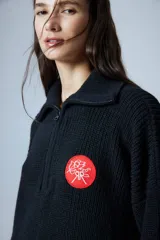 Sweater negro de cuello polo tejido con cierre diente de perro a tono y tajos laterales. Tiene un parche bordado con elementos del drop.