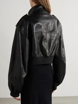 Campera bomber corta de cuero sintético negro, con cuello alto, cierre frontal y detalles de botones metálicos plateados en hombros y bolsillos frontales.