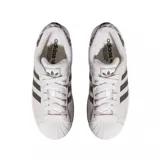 Championes Adidas Superstar de diseño clásico, color blanco con las icónicas tres tiras laterales en tono gris oscuro. Presenta detalle de estampado animal print en el talón y puntera de goma reforzada.