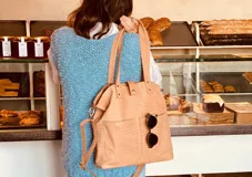 Cartera tipo tote bag color beige con textura símil cocodrilo, doble asa corta y correa larga extraíble y ajustable. Tiene dos bolsillos externos grandes y cierre superior con botón a presión.