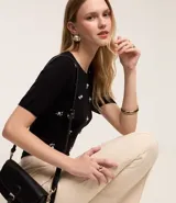 Pantalón flare negro de punto roma con detalle metálico en la cintura y cierre delantero.