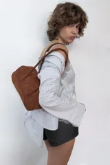Bolso de hombro de formato alargado confeccionado en gamuza color marrón. Cuenta con doble asa de hombro y cierre superior mediante cremallera metálica.