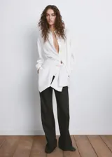 Camisa blanca de lyocell, con cuello solapa, mangas largas y detalle cruzado o de cinturón simulado en la cintura.