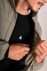 Campera puffer de corte clásico en color beige, con cierre frontal, cuello alto y puños elásticos. Presenta un diseño acolchado horizontal y un pequeño logo bordado en el pecho.