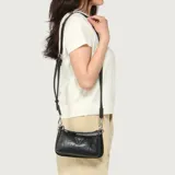 Cartera bandolera Guess modelo Holly de color negro, confeccionada en cuero sintético con estampado en relieve de logotipos de la marca. Cuenta con dos compartimentos principales con cierre superior, herrajes metálicos plateados, un bolsillo frontal con cierre y el distintivo logo triangular de la marca en la parte delantera. Incluye una correa ajustable y desmontable.