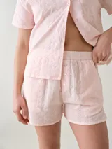 Short de dormir color rosado, confeccionado en broderie de algodón con diseño perforado de flores, cintura elastizada y detalles de botones frontales decorativos.