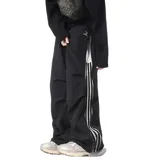 Pantalón deportivo negro de corte muy ancho (baggy) con cierre completo impermeable en los laterales. Presenta tres franjas blancas verticales en el lateral exterior de cada pierna. Posee reguladores en tobillos y cintura.