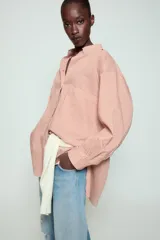 Camisa de cuello solapa y manga larga con estampado de rayas verticales. Presenta un bolsillo de plastrón en el delantero, cierre frontal con botones y detalle de botones en la espalda. Su diseño cuenta con un bajo asimétrico y aberturas laterales.