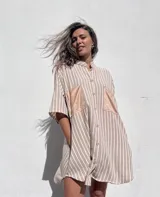 Camisola de corte oversize con estampado de rayas verticales en tonos beige y blanco. Presenta cuello mao, cierre frontal con botones y dos bolsillos delanteros en contraste de material tipo gamuza.