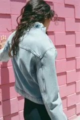 Cazadora de denim color celeste con cuello alto y volantes en el borde frontal. Cuenta con cierre cruzado con botones metálicos y bolsillos en el pecho con solapa.