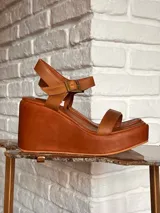 Sandalias de cuero color tostado, con plataforma corrida y taco chino alto, tira delantera fina y tira ajustable al tobillo con hebilla metálica.