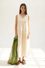 Vestido largo color beige claro, sin mangas, con escote en V y corte escalonado con frunces que le dan volumen.