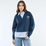 Buzo azul de cuello en V con estampa frontal, que incorpora una camisa de rayas verticales celeste y blanca debajo, creando un efecto de capas.