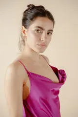 Vestido midi fucsia de satén con escote drapeado, breteles finos y tajo lateral. Presenta una rosa de tela en el bretel izquierdo.