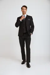 Traje de tres piezas compuesto por saco, chaleco y pantalón de vestir en color negro. El saco presenta solapas clásicas y cierre de botones, el chaleco cuenta con cierre frontal de botones y el pantalón es de corte recto y formal.