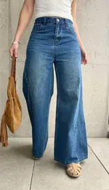 Jean wide leg de tiro medio-alto, color azul con lavado clásico y efecto desgastado. Presenta costuras laterales destacadas que estilizan la silueta, bolsillos delanteros y traseros, y cierre frontal con botón metálico y cremallera.
